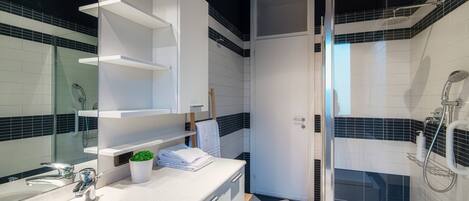A modern bathroom with a glass shower enclosure, a white sink, and a black and white tiled floor.