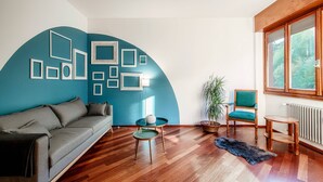 Ein modernes Wohnzimmer mit blauer Akzentwand, Holzböden, einem grauen Sofa, einem runden Glastisch und einem Holzstuhl.