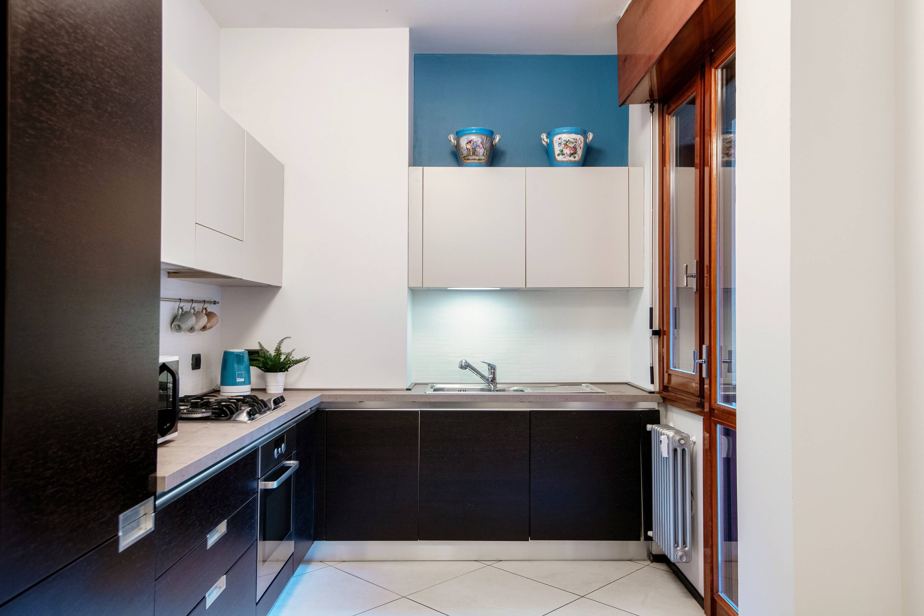 Een kleine keuken met donkere kastjes, een wit aanrechtblad en een blauwe accentmuur.