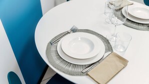 Ein runder Esstisch mit weißer Tischdecke, Besteck und gefaltetem Servietttuch.
