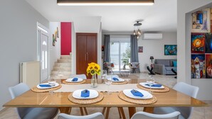 A modern dining area with a glass table set for six, surrounded by white chairs.