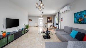 A modern living room with a flat-screen TV, a glass coffee table, a grey sofa, and a painting of parrots.