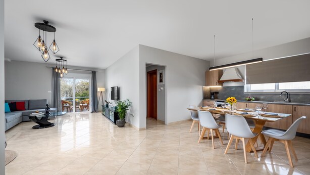 A modern kitchen with a large island, a dining area with a table and chairs, and a living area with a sofa and a coffee table.