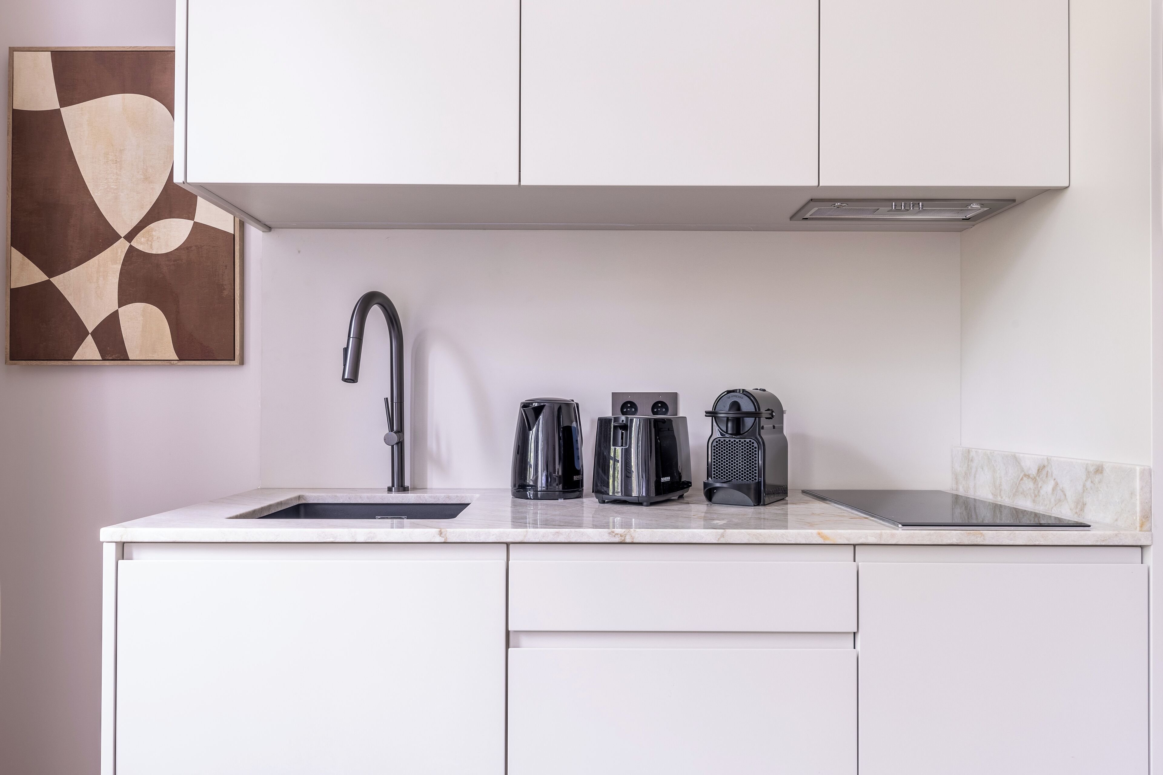 A modern kitchen with white cabinets, a stainless steel faucet, and three coffee makers on the countertop.