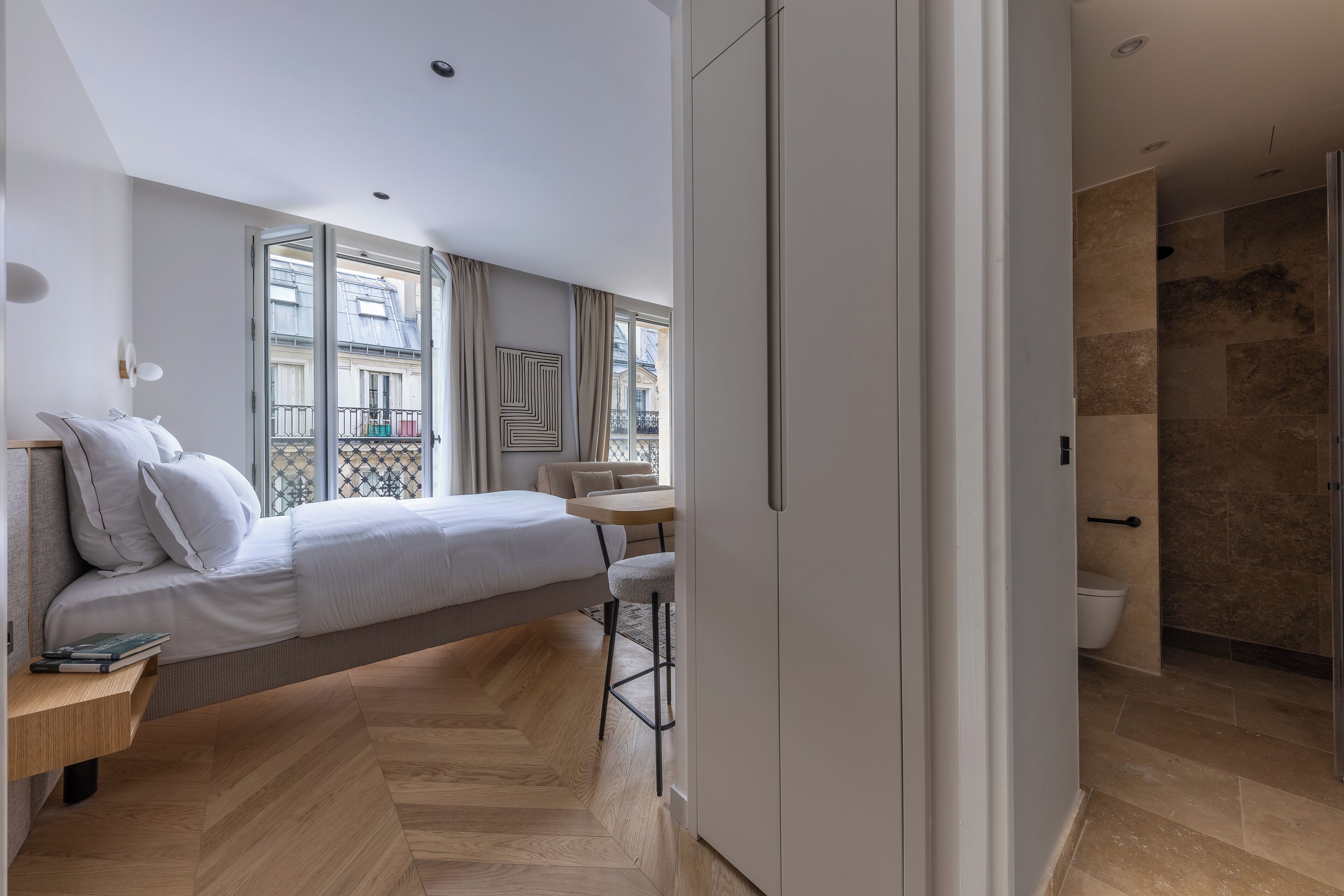 A modern bedroom with a bed, bedside table, and a view of the outside balcony.