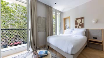 Ein modernes Hotelzimmer mit einem großen Bett, einem kleinen Nachttisch, einem Fenster mit Vorhängen und Blick auf Bäume und Gebäude.