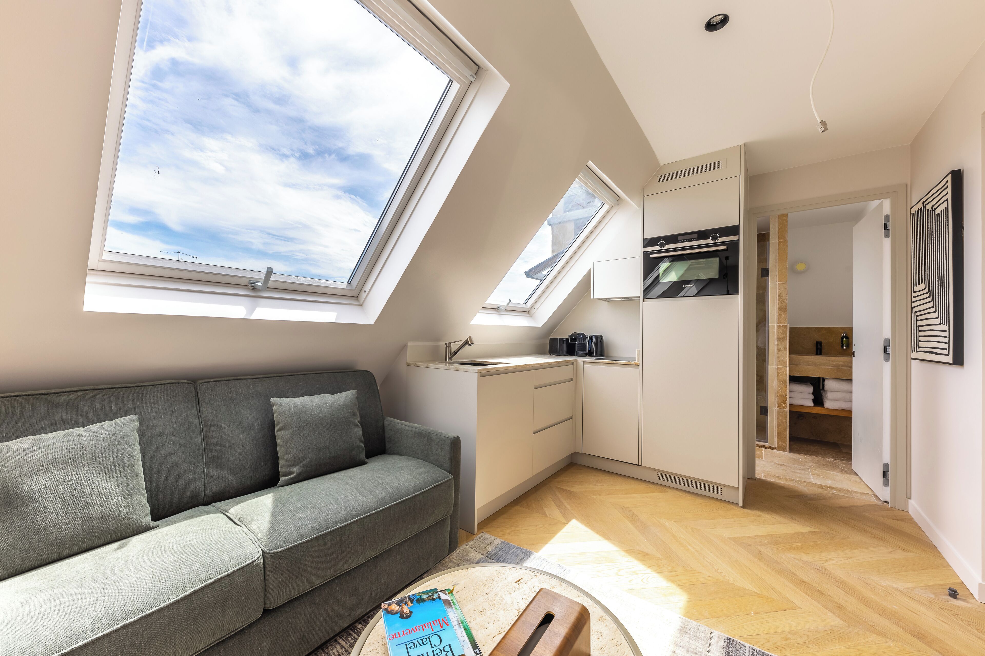 A modern apartment with a grey sofa, skylights, a kitchen, and a visible bathroom.