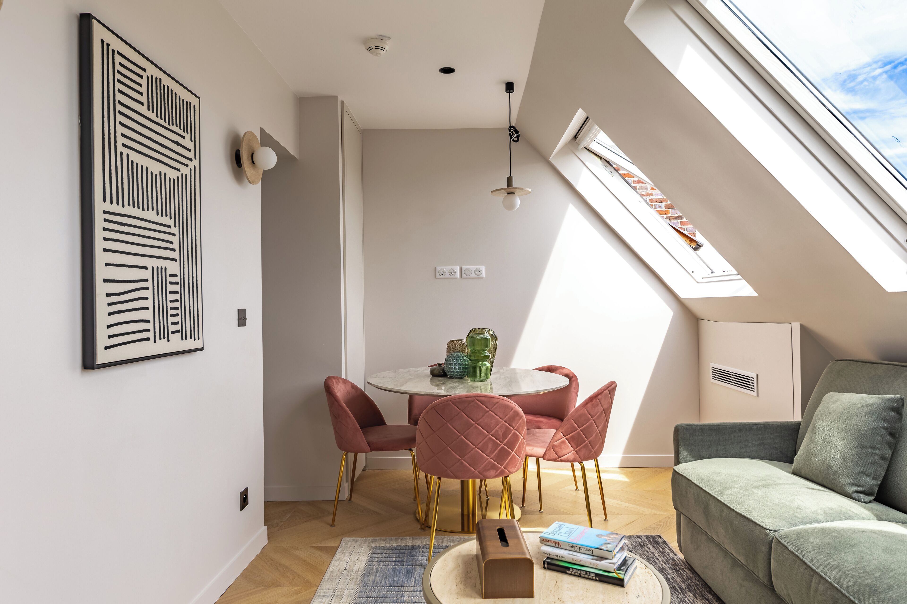 A modern living room with a high ceiling, a dining area with a round table and pink chairs, and a green sofa.