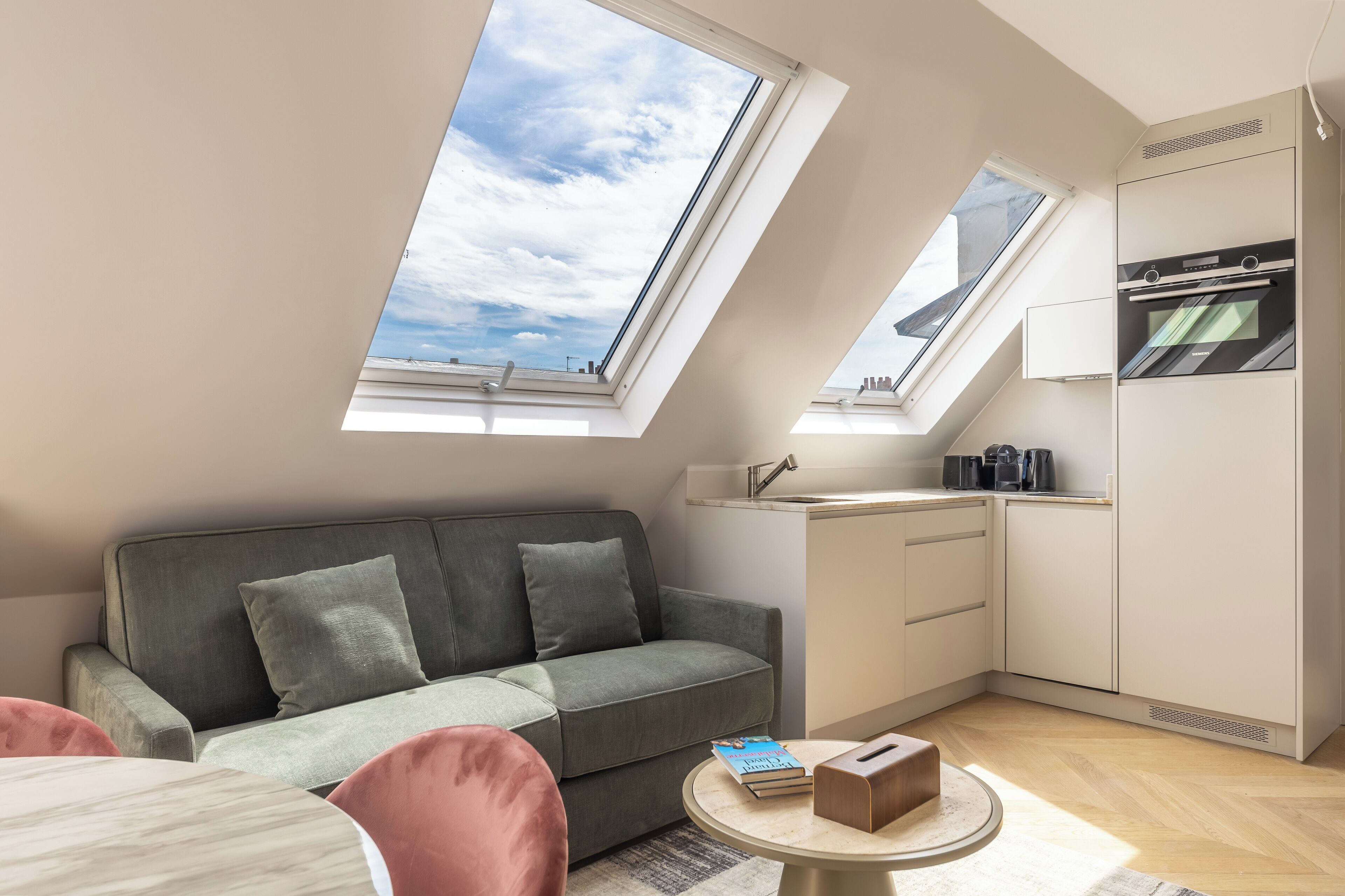 A modern loft bedroom with a skylight, a sofa, a small table, and a kitchenette.