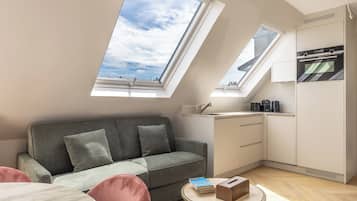 A modern loft bedroom with a skylight, a sofa, a small table, and a kitchenette.