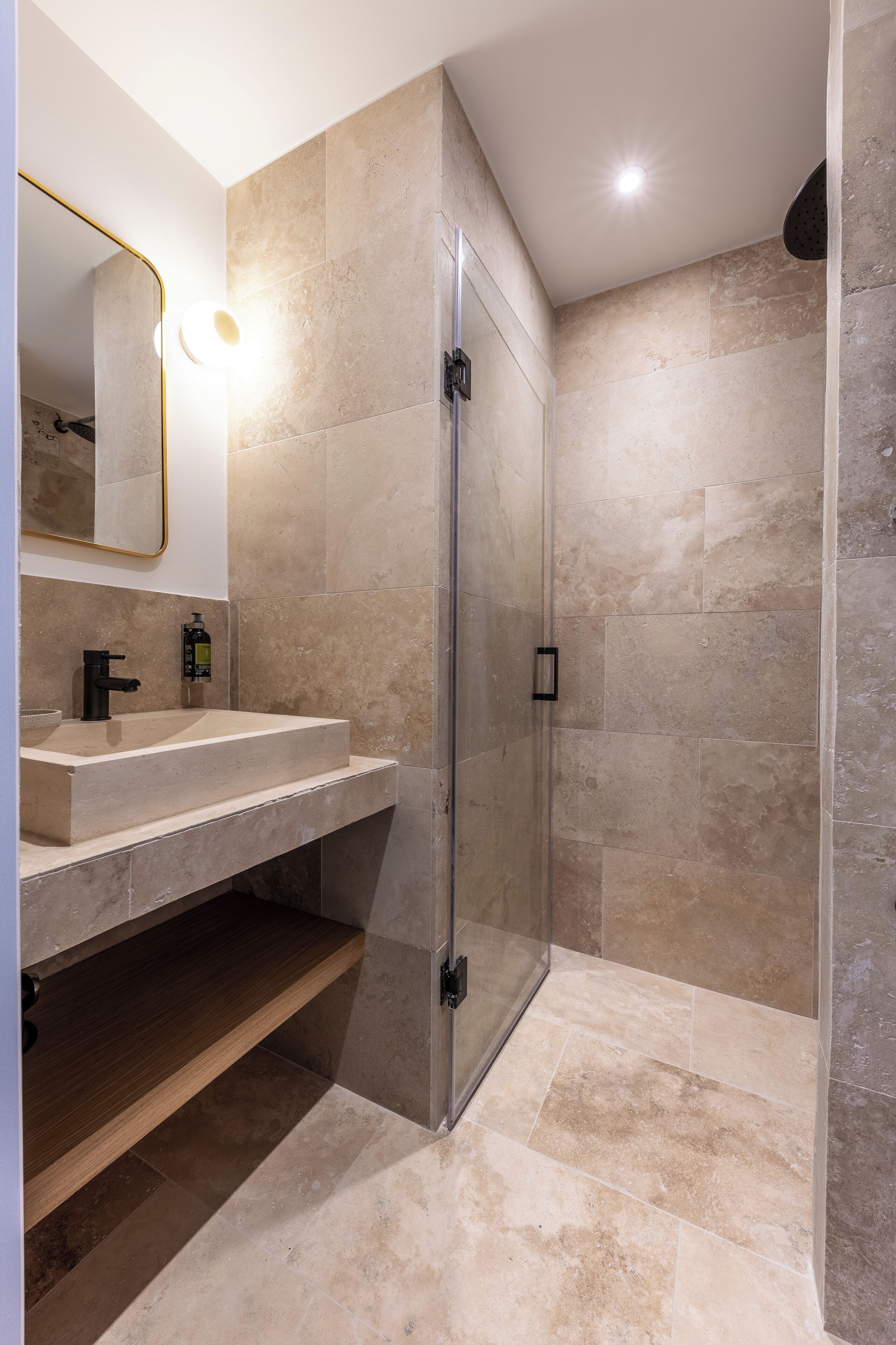 A modern bathroom with a glass shower enclosure, a sink with a mirror, and beige tiles.
