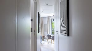 A hallway with a modern design, featuring a light-colored floor, a dining area with a table and chairs, and a view of greenery outside. - Aparthotel Quartier Libre Marais (Paris)