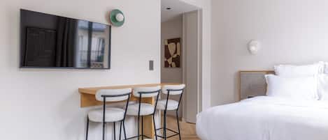 Ein modernes Schlafzimmer mit einem großen Bett, einem an der Wand montierten Fernseher und einer Sitzecke mit Barhocker.
