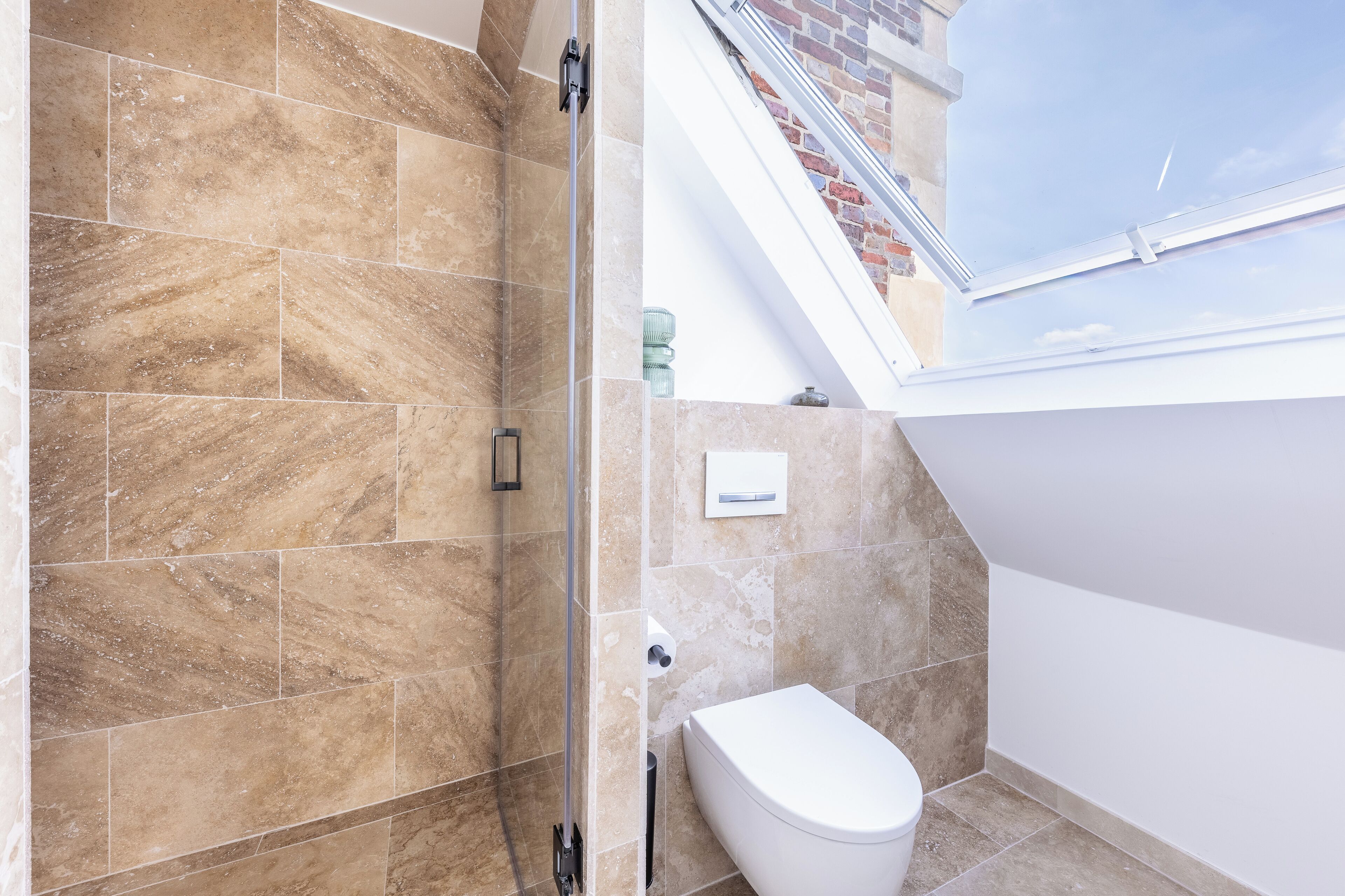 Un baño con ducha, inodoro y tragaluz.