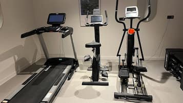 Un gimnasio en casa con una caminadora, una elíptica y una bicicleta estática.