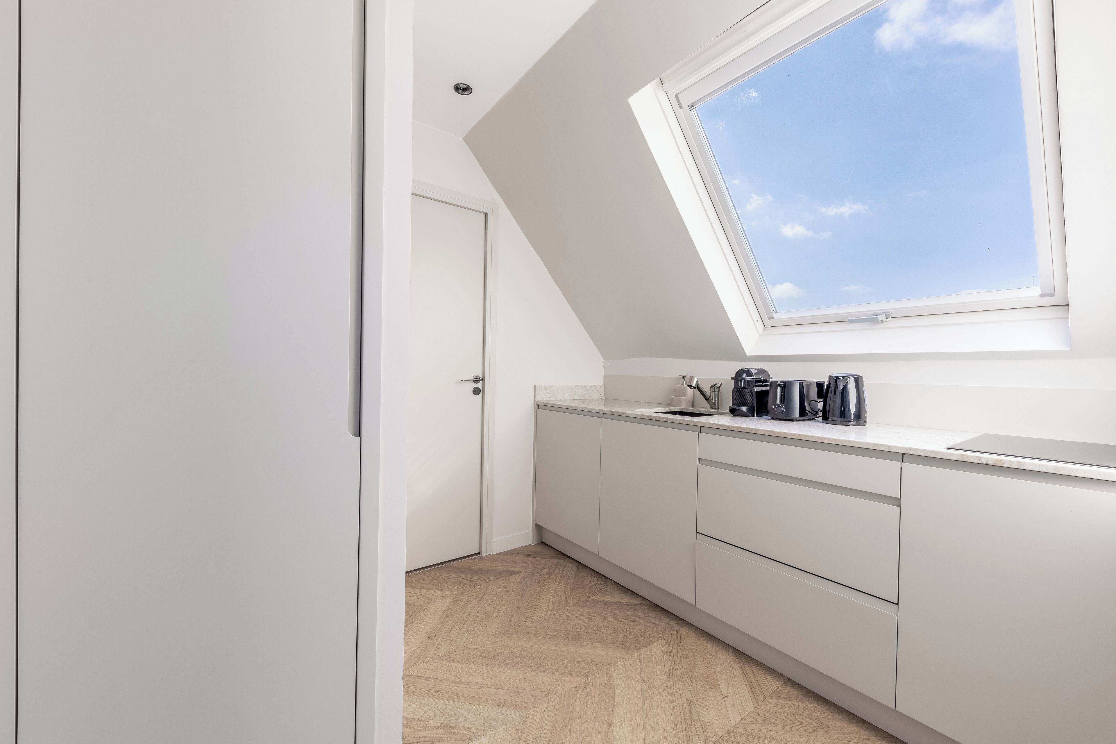 Une cuisine moderne avec des meubles blancs, un puits de lumière et un motif de parquet en chevrons.