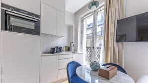 A modern kitchen with a built-in oven and a dining area with a round table and blue chairs. - Aparthotel Quartier Libre Marais (Paris)