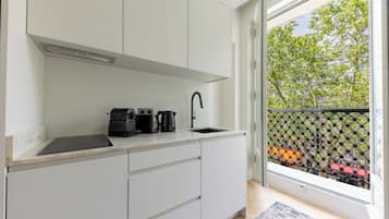 A modern kitchen with white cabinets, a black countertop, and a window with a view of trees and buildings.