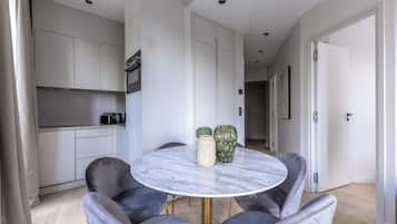 Una cocina moderna con armarios blancos, una zona de comedor con una mesa de mármol y sillas tapizadas en gris.