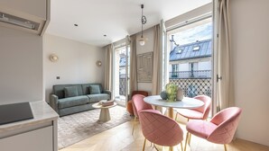 A modern living room with a sofa, a dining table with chairs, and a view of the outside balcony. - Aparthotel Quartier Libre Marais (Paris)