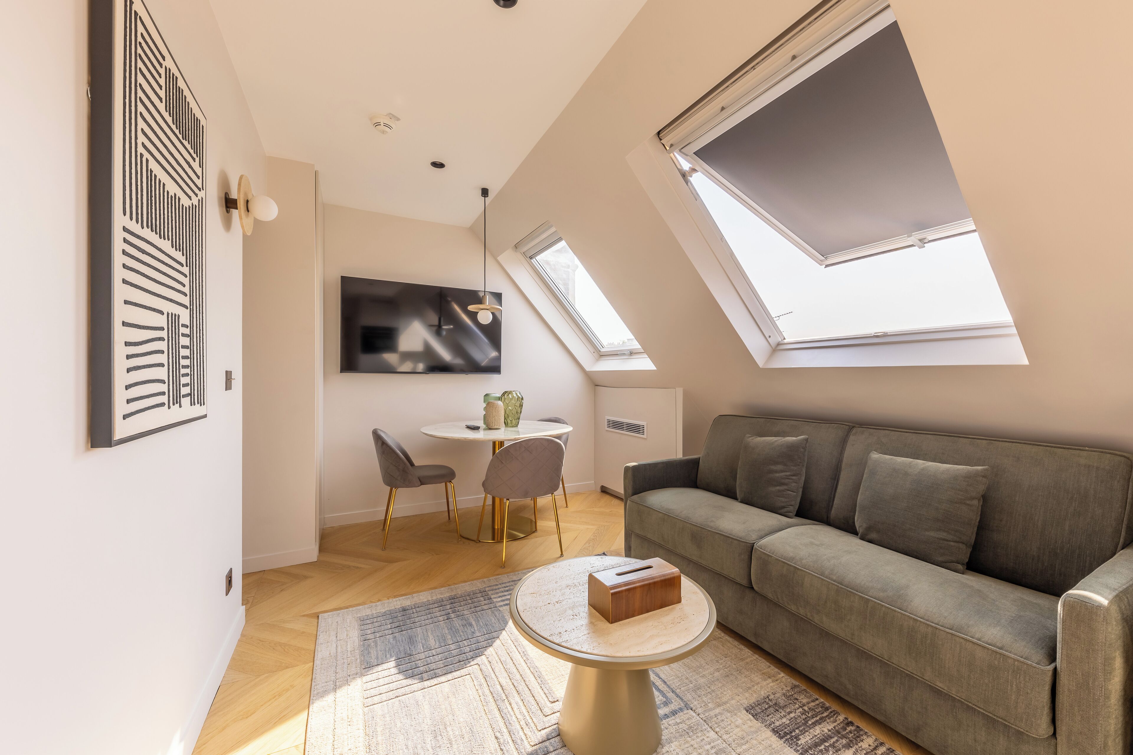 Una sala moderna con un sofá gris, una mesa de centro redonda y un comedor con una mesa y sillas blancas.