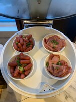 A food steamer with four bowls containing sausages and ham, placed on a kitchen counter.
