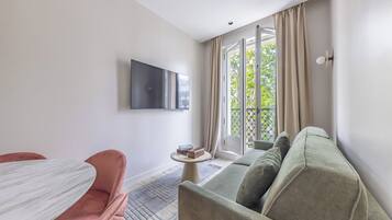 A modern living room with a sofa, a small round table, and a flat-screen TV mounted on the wall.