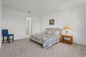 A bedroom with a bed, a chair, a bedside table with a lamp, and a door leading to another room. - Lake-house in WestPalmBeach   (Westlake)
