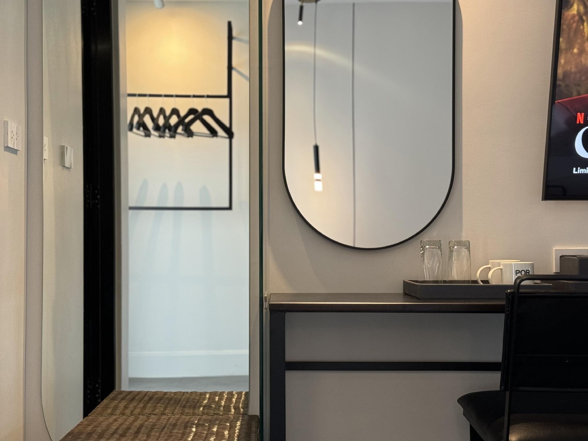 A modern hotel room with a large mirror, a small table with a glass, and a chair.