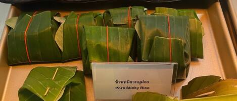 A tray of food items, including wrapped rice and a dish labeled 'Pork Sticky Rice'.
