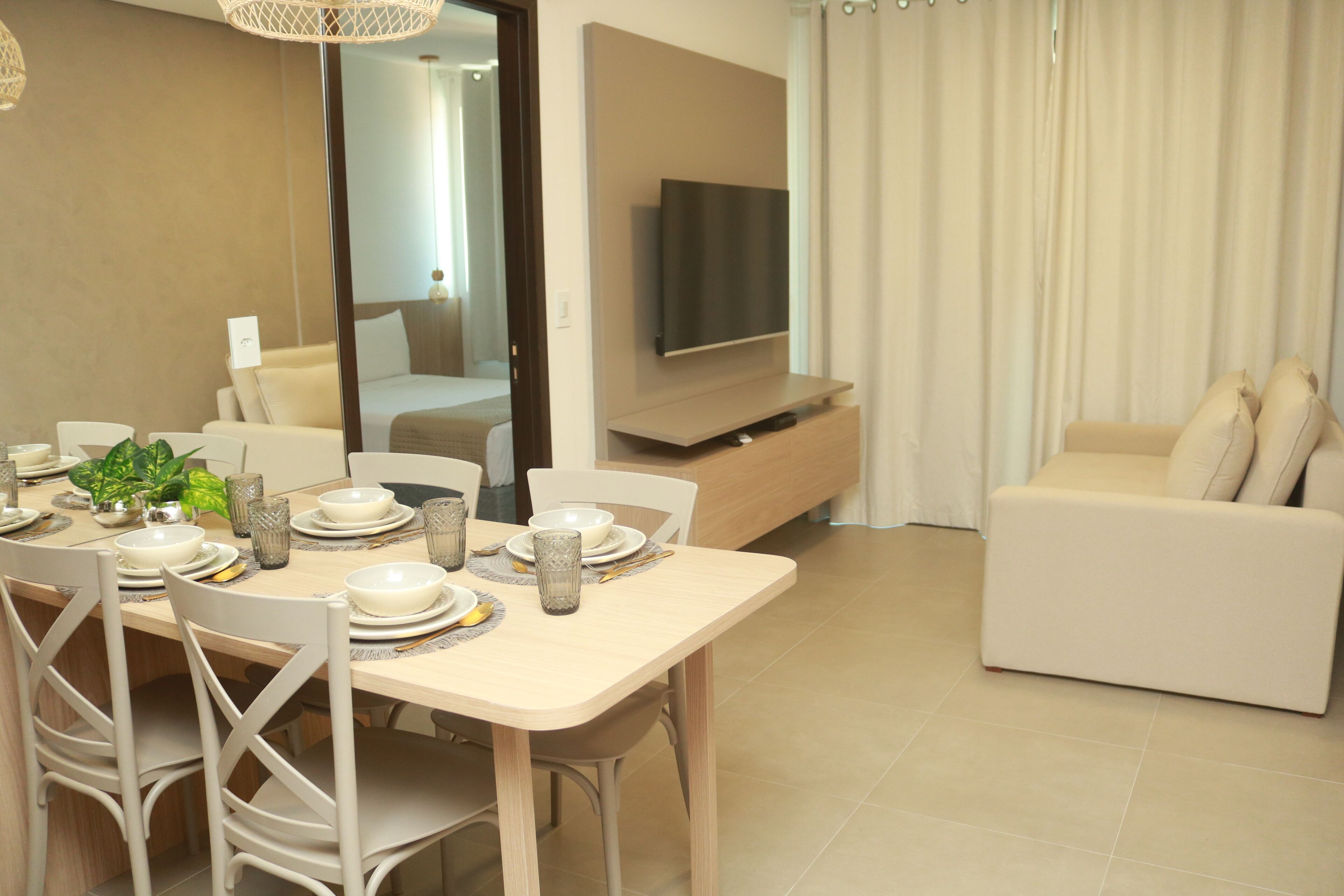 A modern living room with a dining area, a flat-screen TV mounted on the wall, and a beige sofa.