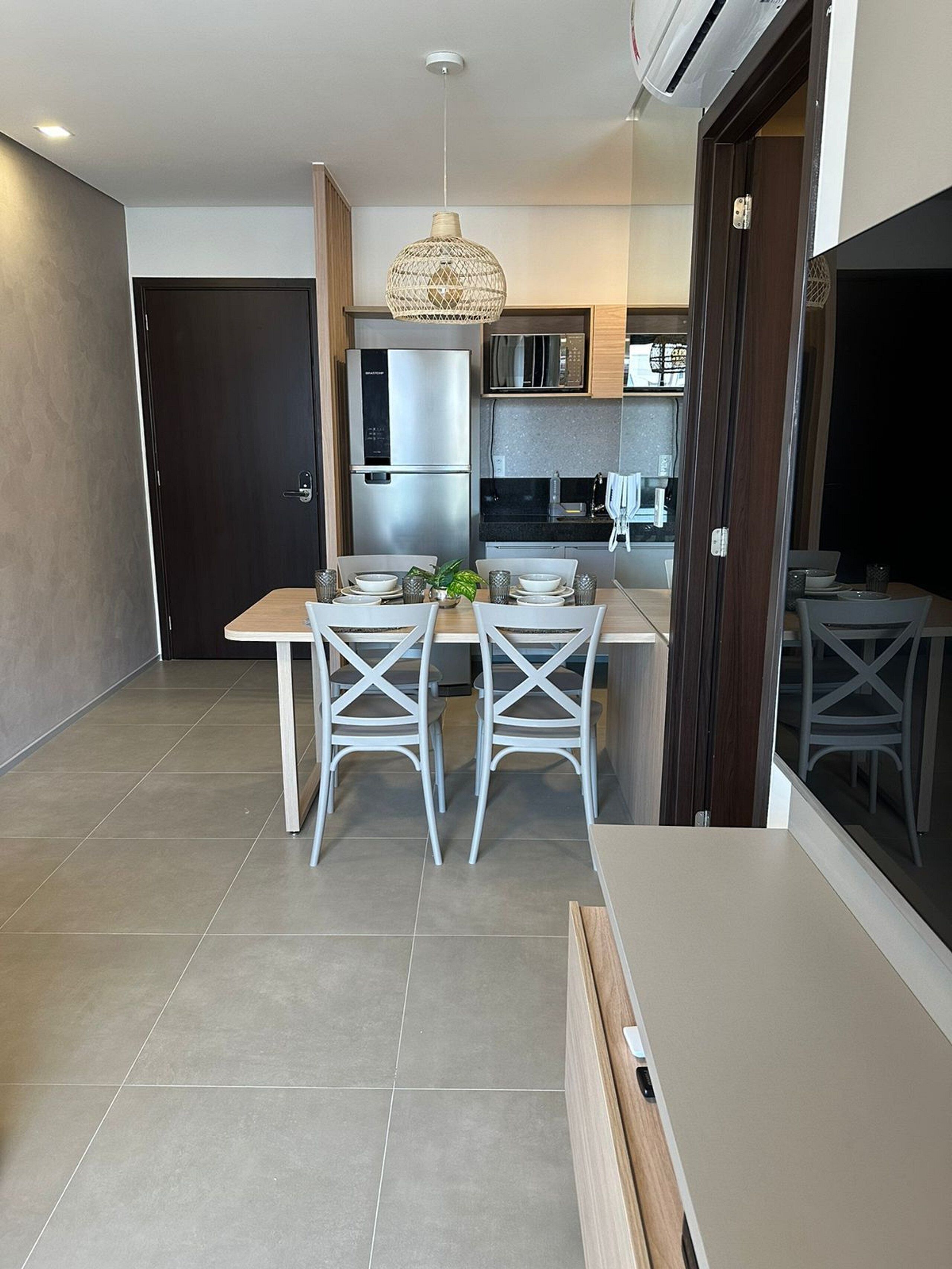 Una cocina moderna con refrigerador, microondas y estufa incorporados. Hay un comedor con mesa y sillas, y una lámpara colgante arriba.