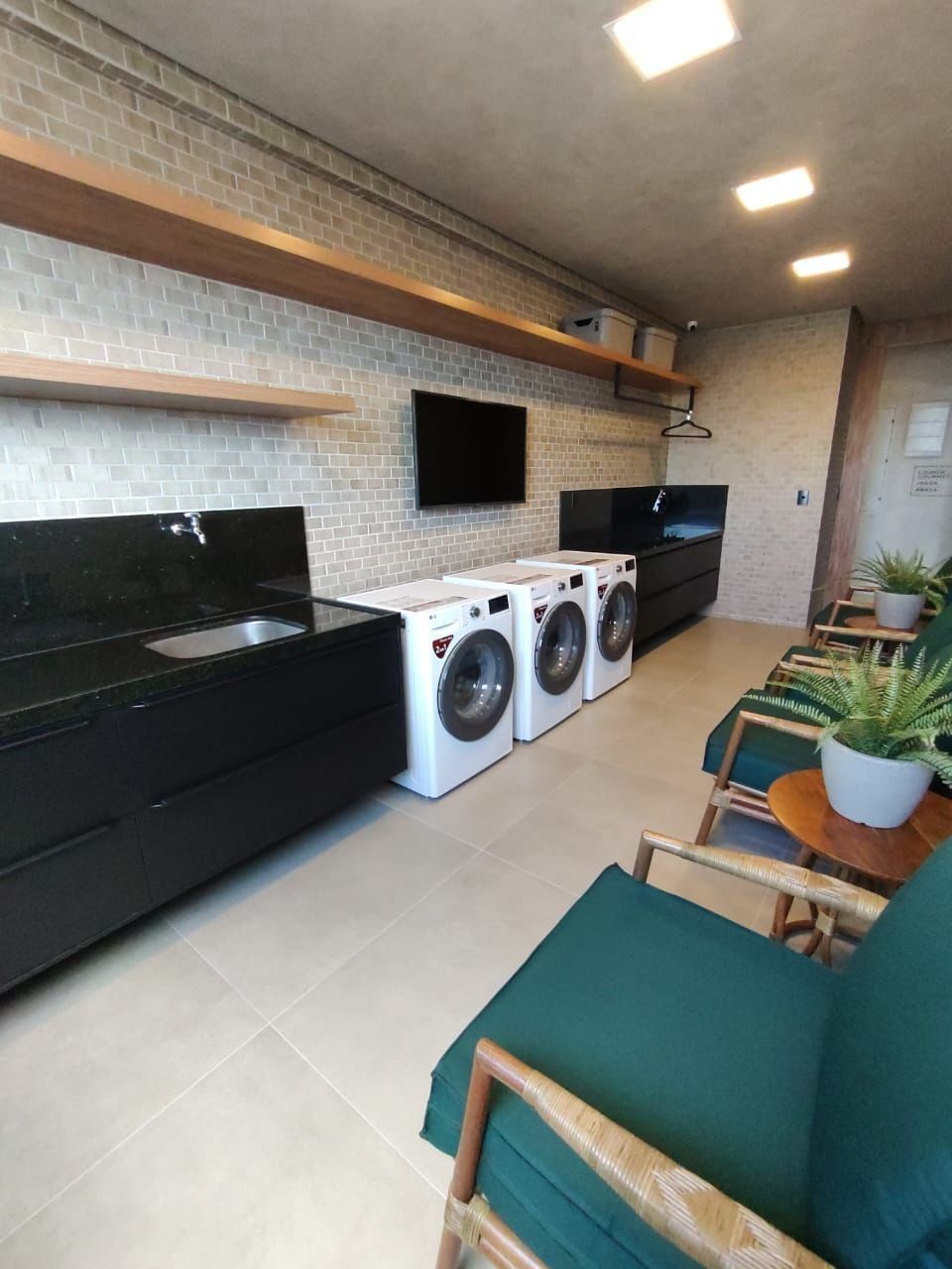 Eine kompakte Küche mit schwarzem Arbeitsplatz, einer eingebauten Waschmaschine und einem flachbildfernseher an der Wand.