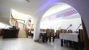 A spacious dining area with high ceilings, a central staircase, and multiple tables and chairs. - Nagar Valley Hotel Ltd. (Dhaka)