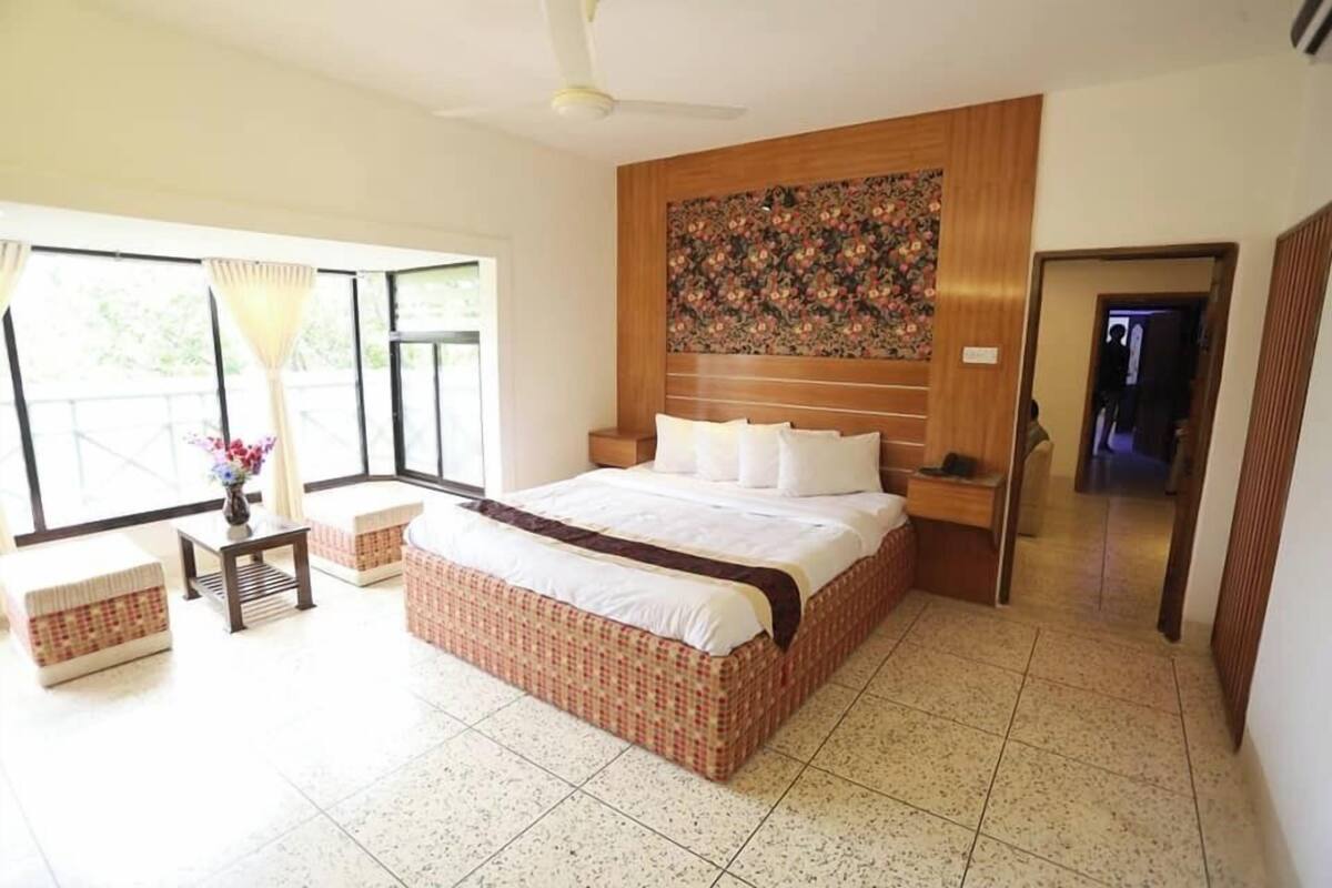 A spacious bedroom with a large bed, a wooden headboard, and a view through large windows.