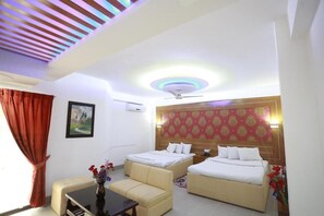 A hotel room with two beds, a sofa, a small table, and a ceiling fan. - Nagar Valley Hotel Ltd. (Dhaka)