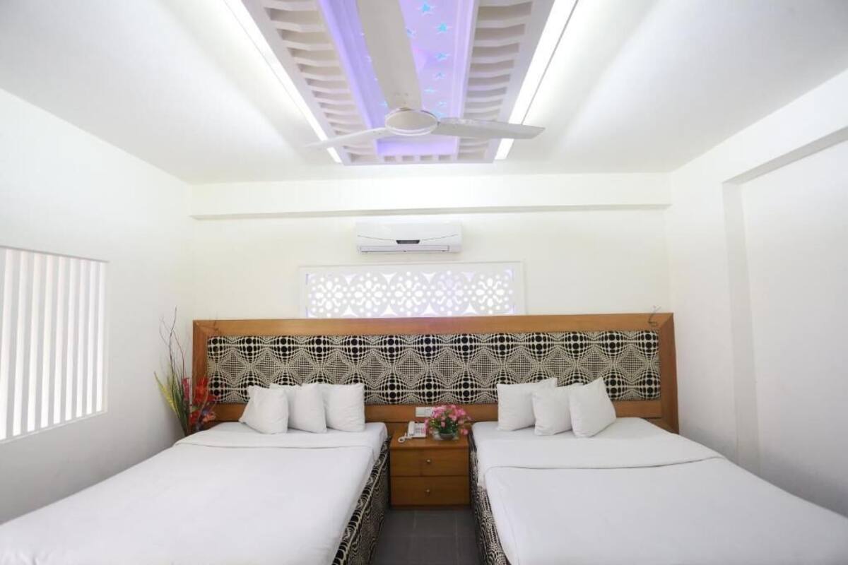 A hotel room with two beds, a ceiling fan, an air conditioning unit, and a decorative wall panel.