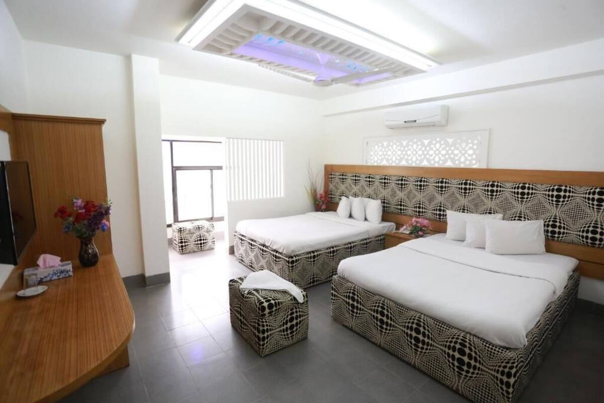 A hotel room with two beds, a wooden desk, and a decorative wall panel.