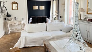 A room with a white sofa, a small wooden table, a decorative lamp, and a model of the Eiffel Tower. - Charmant Appartement en Plein Coeur des Batignolles (Paris)
