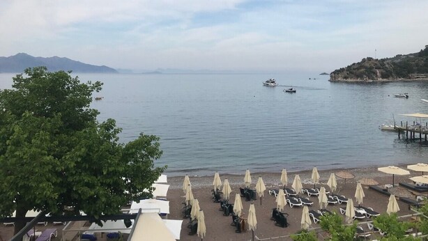 A beach with umbrellas and lounge chairs, a calm sea, and boats in the distance. - Can Apartments (Marmaris)