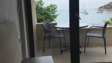 A balcony with a table and two chairs, overlooking a body of water with boats and a hilly landscape.