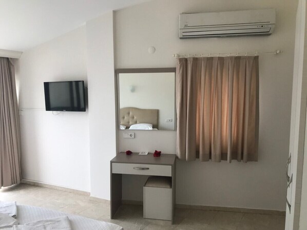 A hotel room with a flat-screen TV mounted on the wall, a small desk with a mirror, a bedside table, and a window with curtains. - Can Apartments (Marmaris)