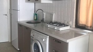 A compact kitchen with a washing machine, a sink, a stove, and cabinets. - Can Apartments (Marmaris)