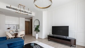A modern living room with a blue sofa, a coffee table, a TV, and a dining area in the background.