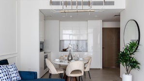 A modern living room with a blue sofa, a dining area with a round table and chairs, and a large mirror on the wall.