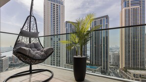 A balcony with a hanging chair and a potted plant, overlooking a cityscape with tall buildings.