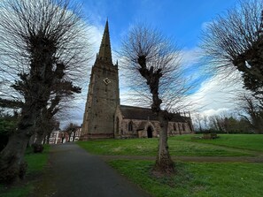 A church with a tall spire, a pathway leading to the entrance, and a grassy area with trees. - 2-bed Apartment in Coleshill (Birmingham)