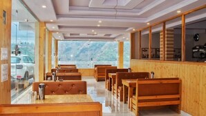 A restaurant with wooden benches and tables, large windows, and a view of the mountains. - The Bel Mount (Dhanaulti)