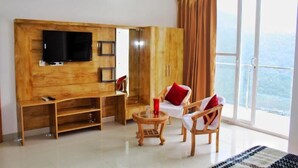 A room with a TV mounted on a wooden wall, a sofa, two chairs, a small table, and a large window with a view. - The Bel Mount (Dhanaulti)