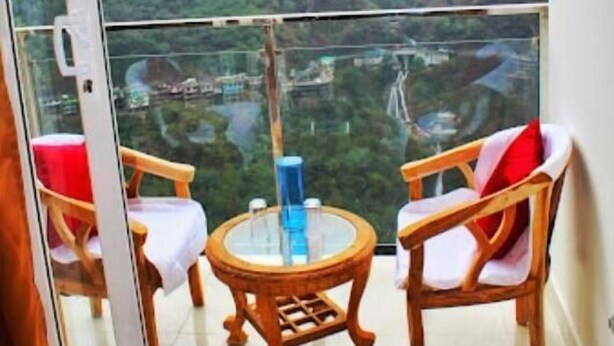 A balcony with two wooden chairs and a small round table, overlooking a mountainous landscape with a view of a valley and a bridge. - The Bel Mount (Dhanaulti)
